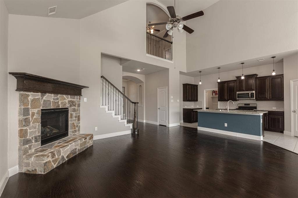 1742 Amalfi Drive, McLendon Chisholm, TX 75032 High-ceiling interior featuring a floor-to-ceiling stone fireplace with a wood mantel, dark wood-finish flooring, a tiered kitchen island with quartz countertops, custom wood cabinetry, and an open loft landing with metal balusters