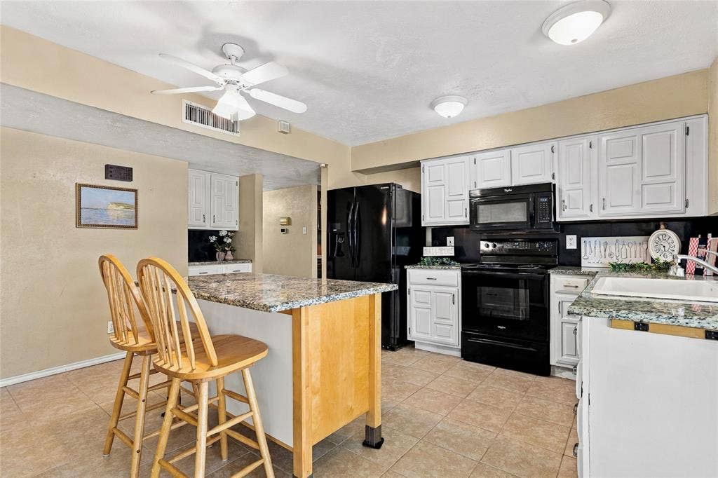1901 Dodge Trail, Grand Prairie, TX 75052 Kitchen featuring white cabinetry, black appliances, a center island with seating, and ample counter space.