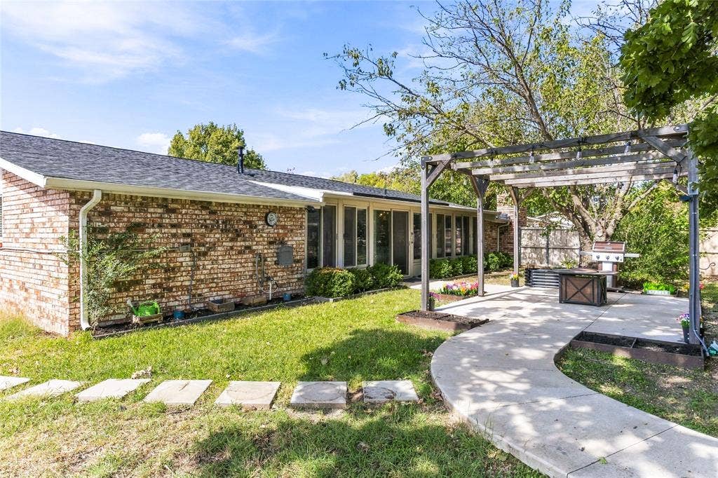 1901 Dodge Trail, Grand Prairie, TX 75052 Backyard view showcasing the brick exterior, covered patio area, storage shed, mature trees, and grassy lawn.