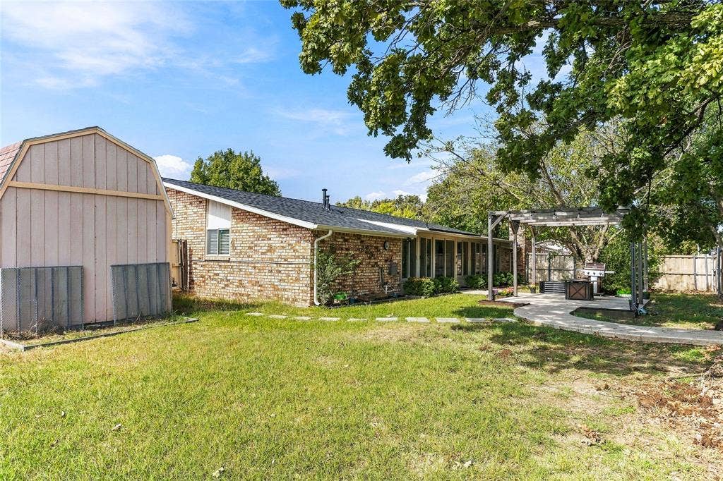 1901 Dodge Trail, Grand Prairie, TX 75052 Backyard featuring a curved concrete walkway, covered patio, brick exterior, and established landscaping.