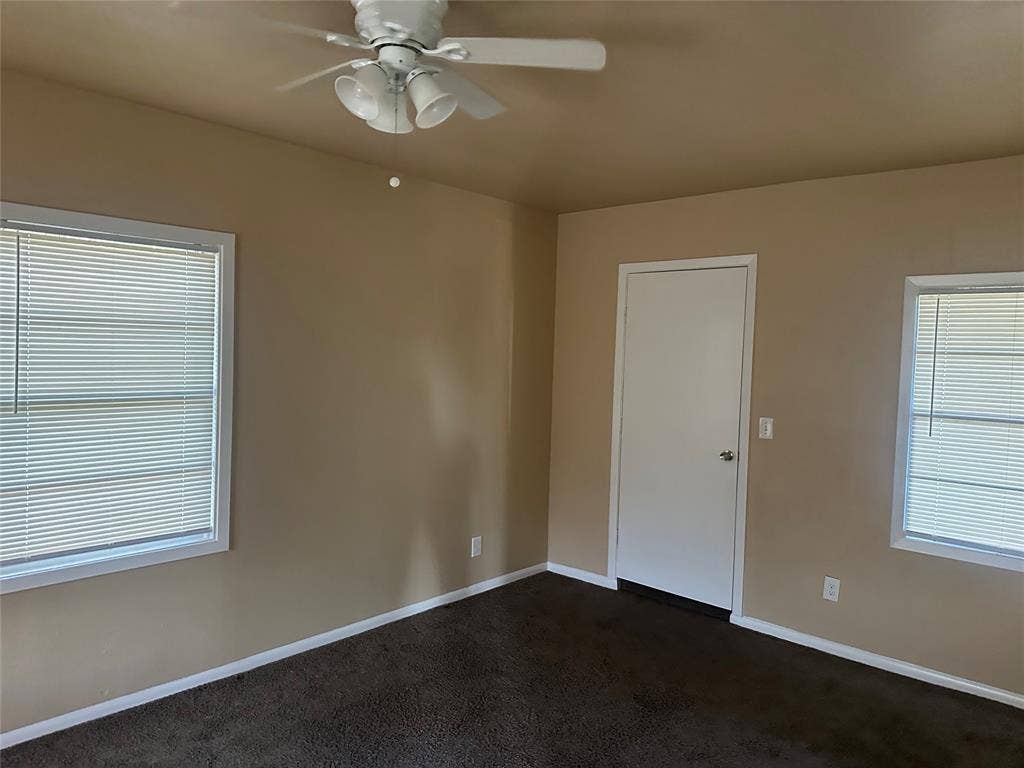 11809 Oberlin Drive, Dallas, TX 75243 Neutral-toned room featuring dark carpeting, two windows with horizontal blinds, and a white ceiling fan with integrated lighting