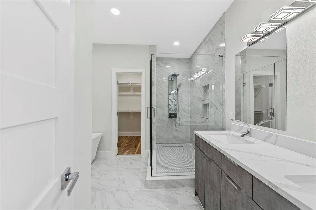 2503 Crossman Avenue, Dallas, TX 75212 Bathroom featuring a dual-sink vanity with a solid-surface countertop, a walk-in shower with floor-to-ceiling stone-pattern tile, a ceiling-mounted shower panel system, and recessed lighting