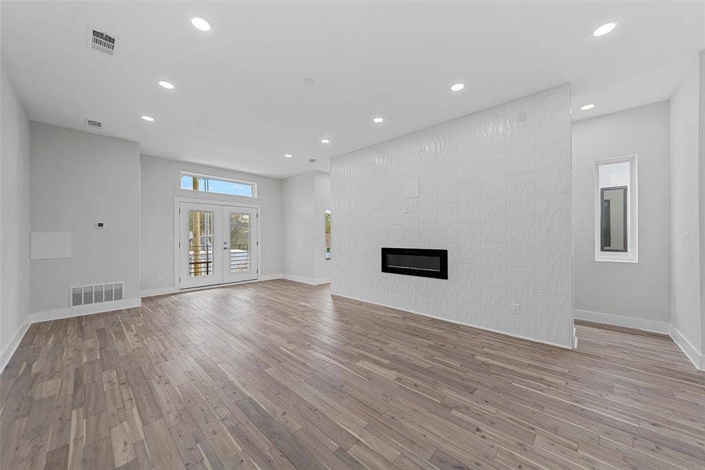 2503 Crossman Avenue, Dallas, TX 75212 Interior space featuring wood-finish flooring, recessed lighting, double glass-paneled doors, and a floor-to-ceiling accent wall with an integrated linear fireplace