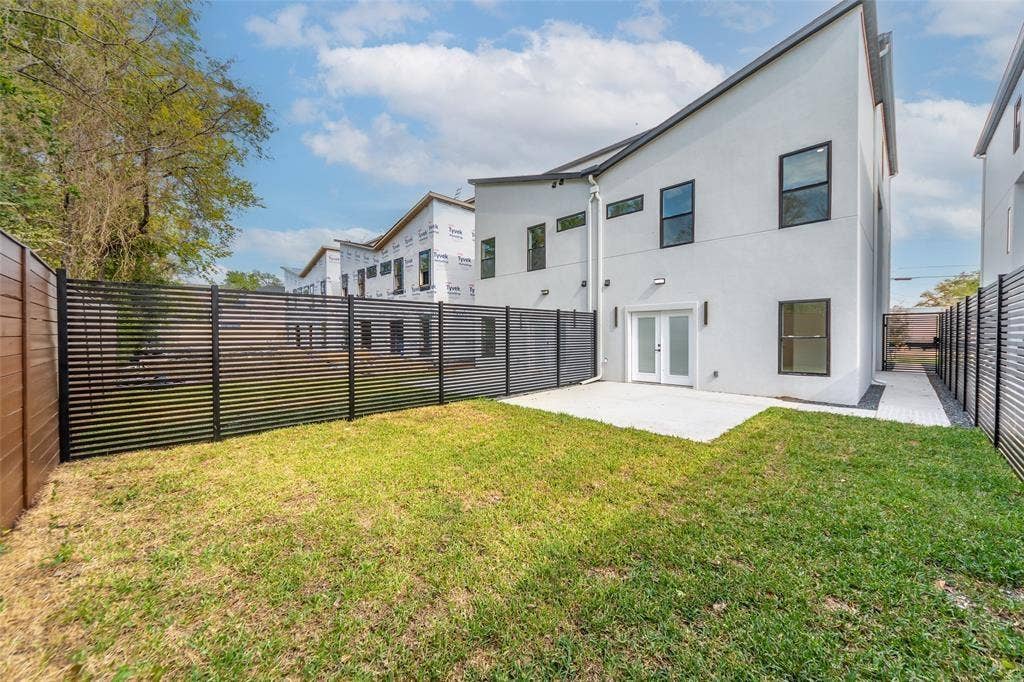 2503 Crossman Avenue, Dallas, TX 75212 Contemporary white exterior with dual-pitched rooflines, featuring a concrete patio, horizontal slat perimeter fencing, and manicured turf