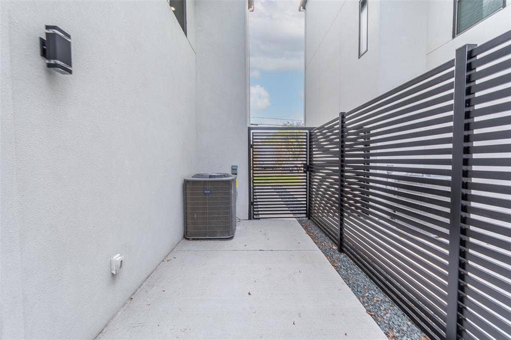2503 Crossman Avenue, Dallas, TX 75212 Side yard featuring smooth stucco walls, black metal horizontal-slat fencing, a concrete walkway, and wall-mounted exterior lighting