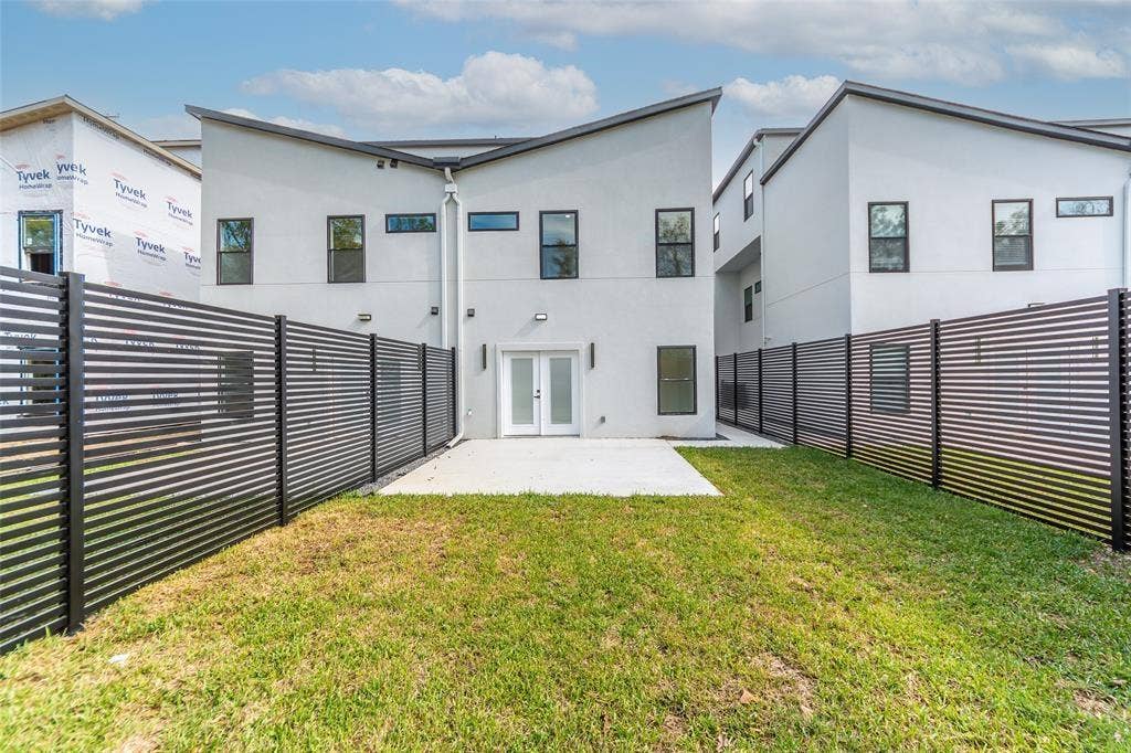 2503 Crossman Avenue, Dallas, TX 75212 Modern two-story exterior featuring light-toned stucco siding, a sharp shed roofline, black horizontal slatted perimeter fencing, a concrete rear patio, and dual-pane glass entry doors