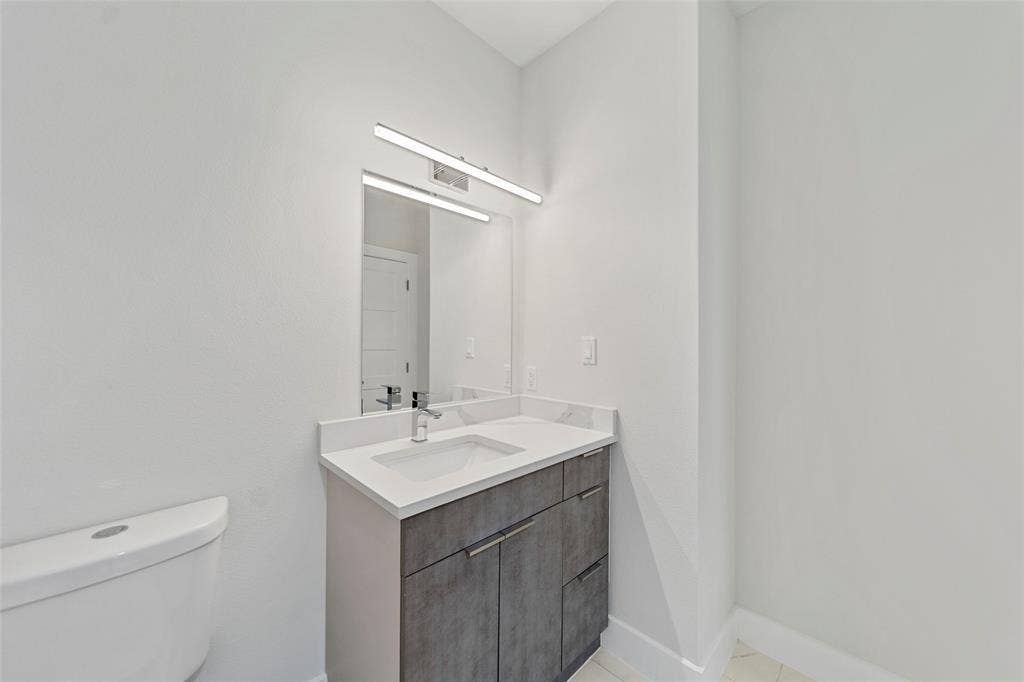 2503 Crossman Avenue, Dallas, TX 75212 Modern vanity featuring a stone-composite countertop, rectangular undermount sink, chrome faucet, grey textured cabinetry, and wall-mounted linear LED lighting