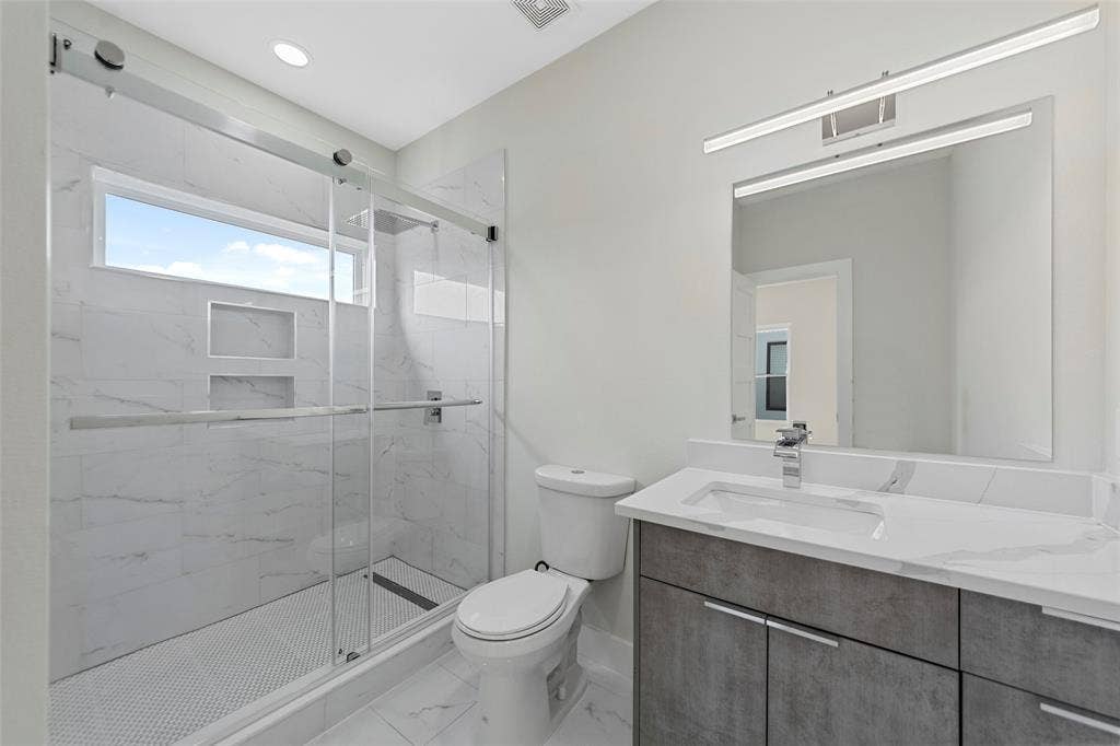 2503 Crossman Avenue, Dallas, TX 75212 Bathroom featuring a vanity with stone-finish countertop, walk-in shower with sliding glass doors, dual recessed shower niches, and polished chrome fixtures