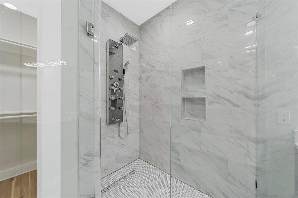2503 Crossman Avenue, Dallas, TX 75212 Walk-in shower featuring floor-to-ceiling stone-finish tile, recessed wall shelving, a stainless steel multi-head rainfall shower panel, and a mosaic tile floor with linear drain, enclosed by a frameless glass partition