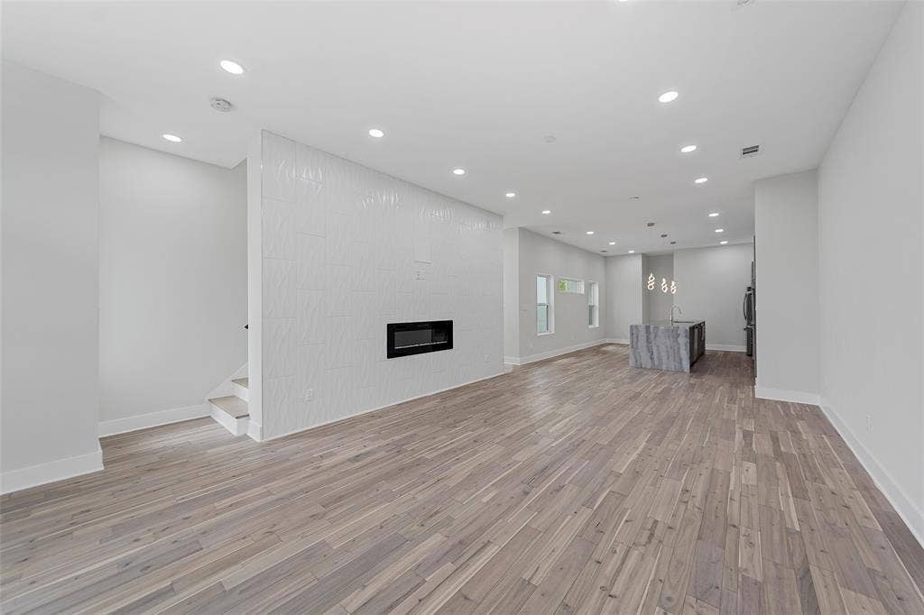 2503 Crossman Avenue, Dallas, TX 75212 Open floor plan featuring wood-finish flooring, recessed lighting, a fireplace with a textured accent wall, and a kitchen island with stone-finish surfaces