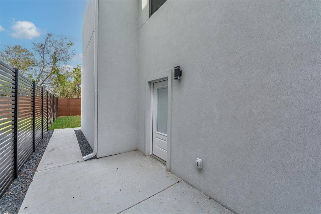 2503 Crossman Avenue, Dallas, TX 75212 Smooth stucco exterior featuring a single-panel glass-insert entry door, concrete pathway, decorative gravel border, and horizontal slat privacy fencing