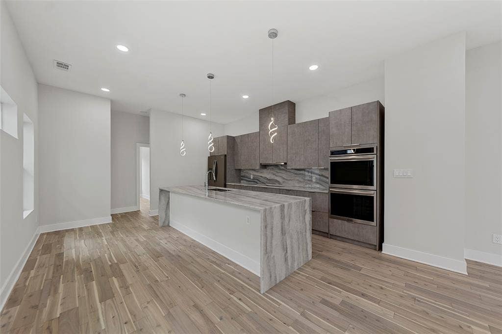 2503 Crossman Avenue, Dallas, TX 75212 Kitchen featuring a waterfall-edge island, wood-finish flooring, recessed lighting, double wall ovens, and custom cabinetry