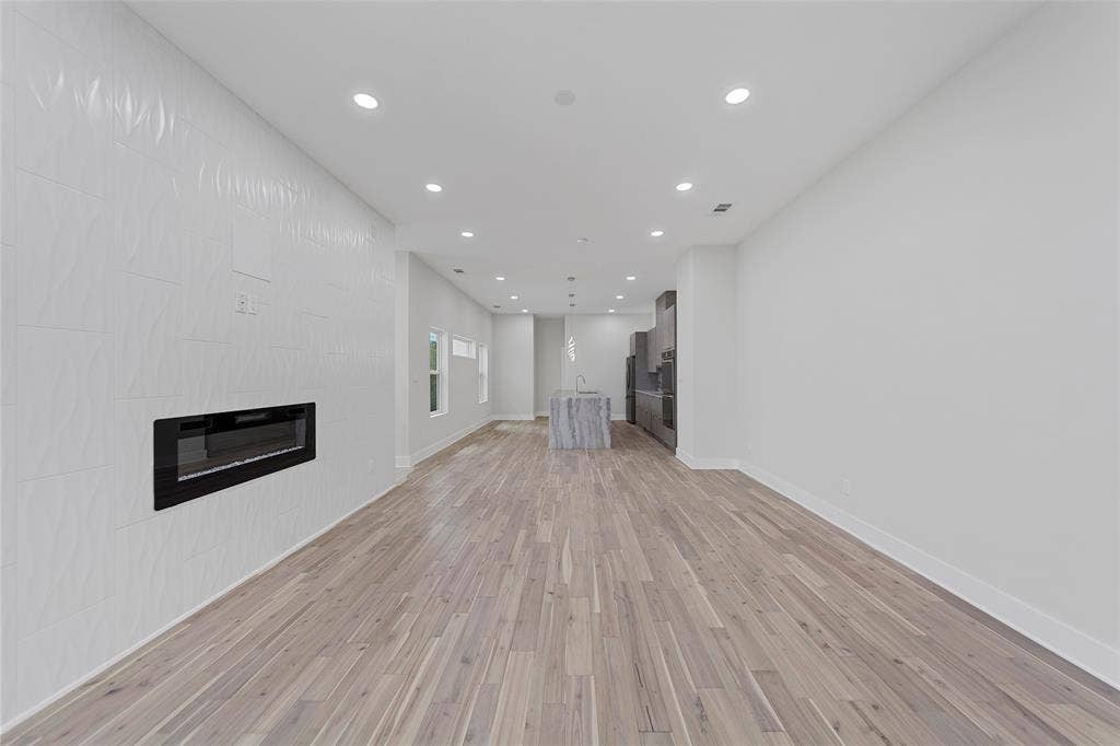 2503 Crossman Avenue, Dallas, TX 75212 Open-concept interior featuring wood-finish flooring, recessed lighting, a built-in electric fireplace with a textured surround, and a center island with stone-finish surfaces