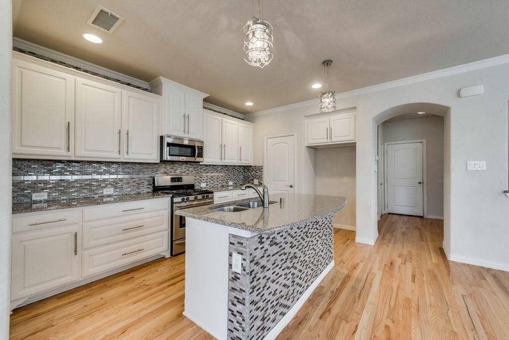 636 S Greenville Avenue, Richardson, TX 75081 Kitchen featuring decorative light fixtures, a center island with sink, appliances with stainless steel finishes, white cabinetry, and light stone counters