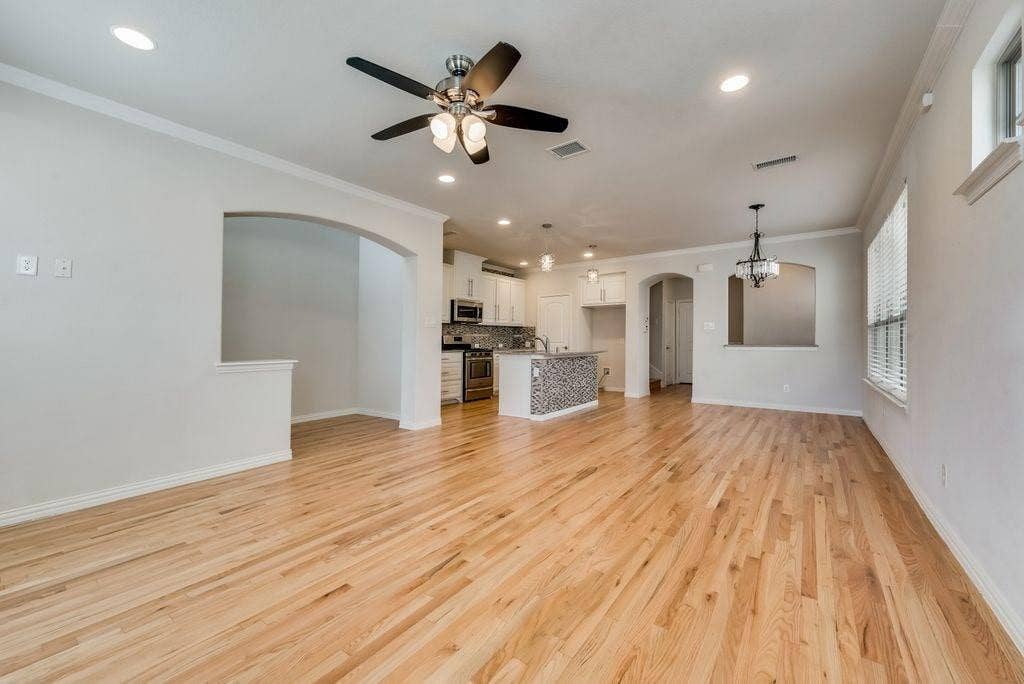 636 S Greenville Avenue, Richardson, TX 75081 Unfurnished living room featuring plenty of natural light, ornamental molding, and ceiling fan with notable chandelier
