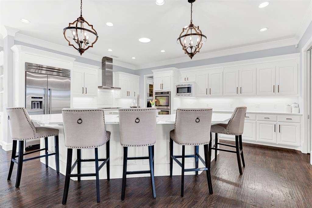 2608 LAWTON Lane, Plano, TX 75093 Sculpted lantern pendants cast a warm, welcoming light over the wide curved breakfast bar and custom white cabinetry. It is the perfect spot for casual weekday breakfasts or chatting with family while putting the finishing touches on a meal.