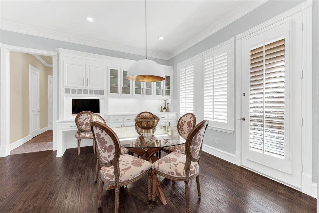 2608 LAWTON Lane, Plano, TX 75093 Plantation shutters filter soft morning sun across a custom office alcove and glass-front display cabinetry. Imagine starting your day checking early emails with a fresh cup of coffee right beside the sunny side yard view.