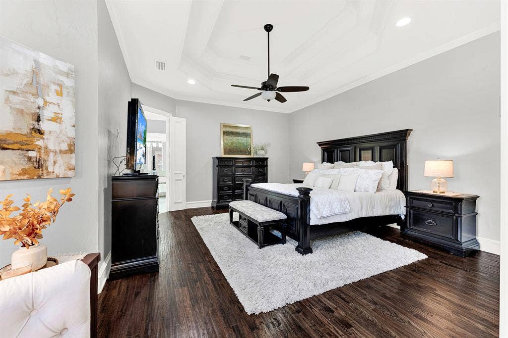 2608 LAWTON Lane, Plano, TX 75093 A multi-tiered tray ceiling adds architectural depth above, creating a grand sense of volume over rich, dark wood flooring. Picture sinking into fresh linens at the end of a long day, wrapped in quiet comfort and total peace.