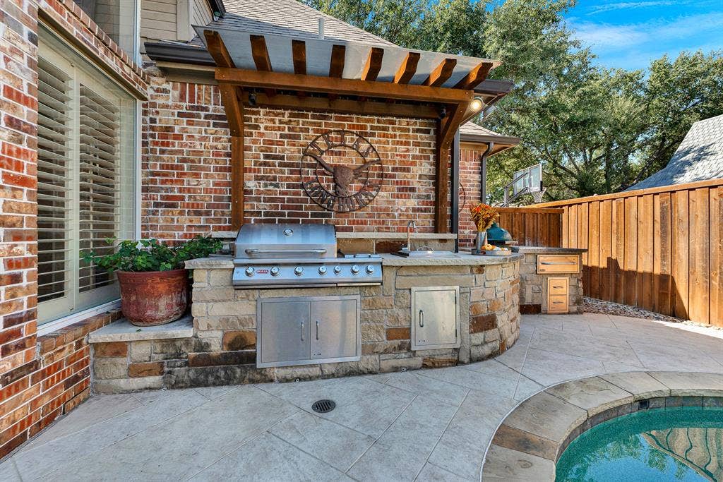 2608 LAWTON Lane, Plano, TX 75093 A built-in stone grill station sits sheltered under a custom timber arbor along the brick exterior wall. Picture sizzling up fresh steaks and appetizers while chatting with friends gathered poolside on warm summer evenings.