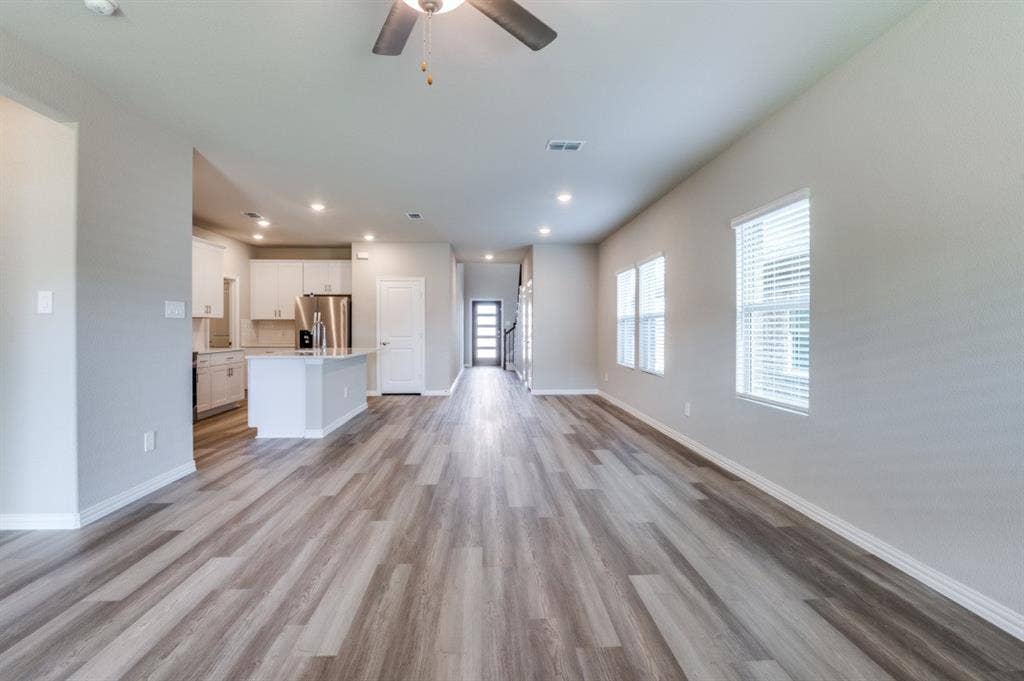 Open-concept interior featuring wood-finish flooring, recessed lighting, white cabinetry, a kitchen island with stone countertop, and large windows with blinds