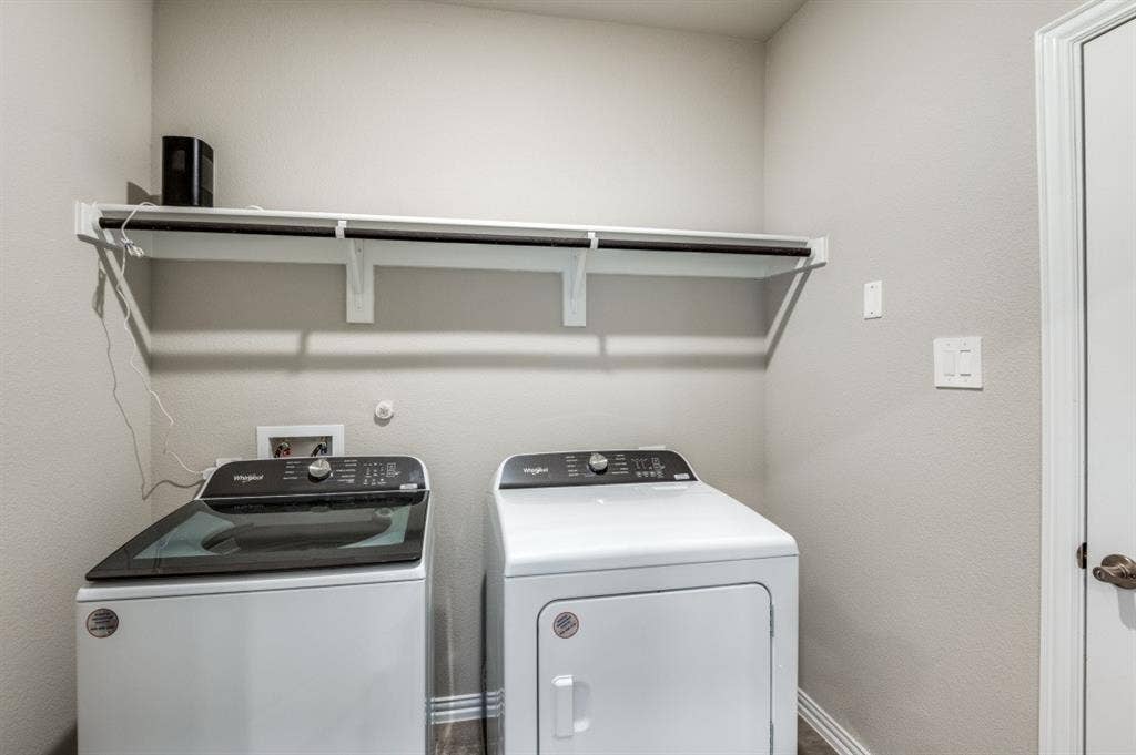Utility area featuring neutral wall paint, white Whirlpool washer and dryer, and a built-in wall-mounted shelving unit with an integrated hanging rod