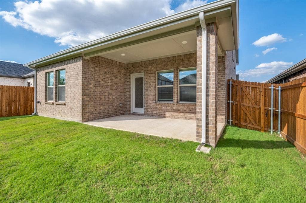 Brick exterior featuring a covered rear patio, recessed lighting, and a fenced backyard with grass lawn