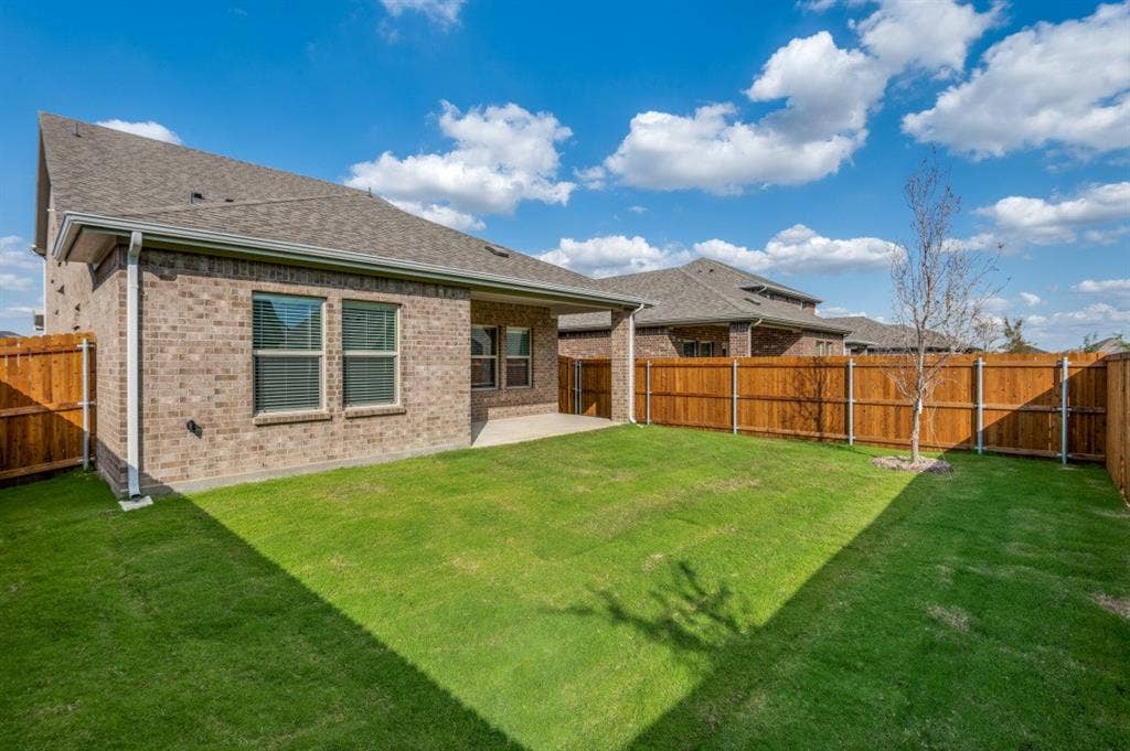 Rear exterior featuring brick masonry, a covered concrete patio, and a fenced backyard with a lawn