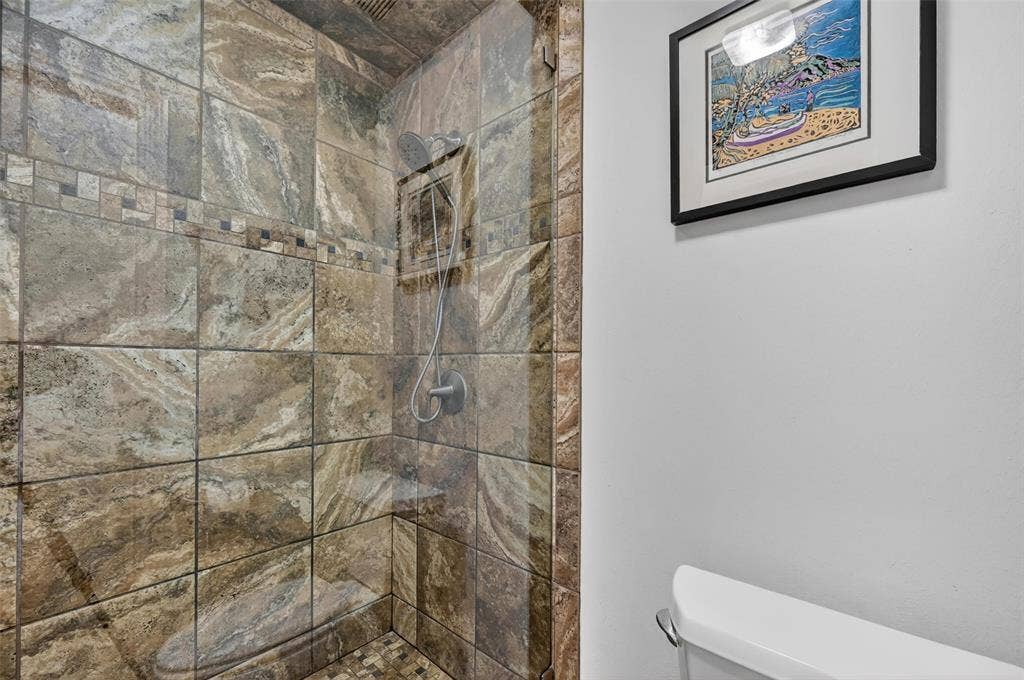 12627 Breckenridge Drive, #200, Dallas, TX 75230 Walk-in shower featuring floor-to-ceiling stone-finish wall tiles, an integrated corner shelving unit, a frameless glass enclosure, and a handheld showerhead