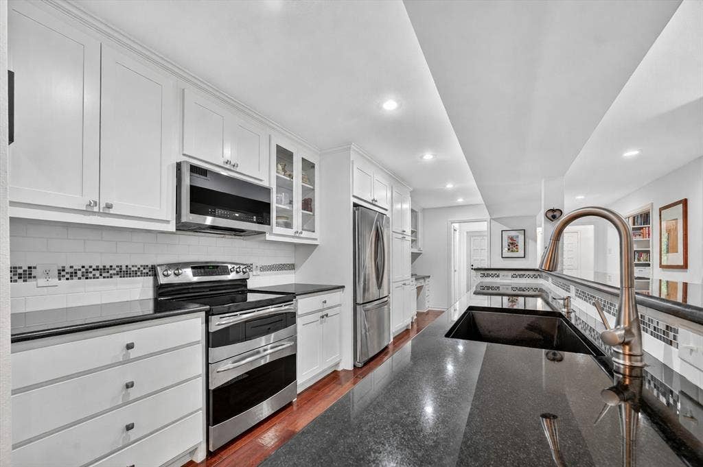 12627 Breckenridge Drive, #200, Dallas, TX 75230 Kitchen featuring white shaker-style cabinetry, polished dark countertops, stainless steel appliances, subway tile backsplash with glass mosaic accents, and wood-finish flooring