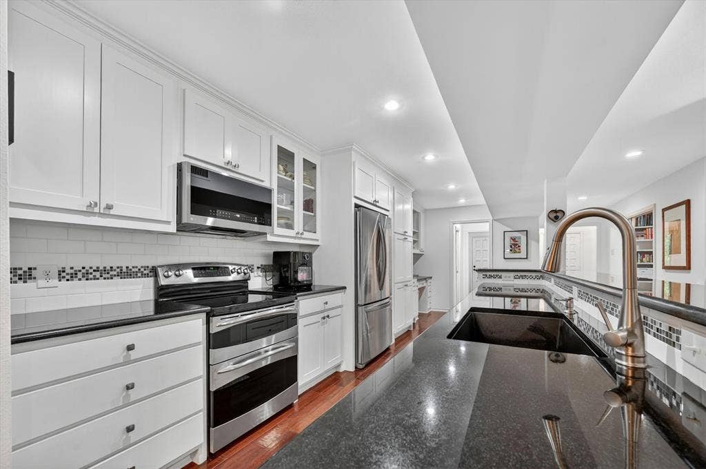 12627 Breckenridge Drive, #200, Dallas, TX 75230 Kitchen featuring white shaker-style cabinetry, dark stone countertops, stainless steel appliances, a mosaic tile backsplash, and wood-finish flooring