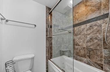 12627 Breckenridge Drive, #200, Dallas, TX 75230 Walk-in shower enclosure featuring floor-to-ceiling neutral tile, a built-in recessed shelf, a glass sliding door, and integrated jetted tub