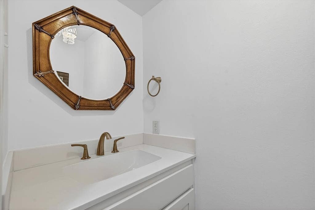 12627 Breckenridge Drive, #200, Dallas, TX 75230 Solid surface vanity with an integrated basin, brass-finish widespread faucet, wall-mounted circular decorative mirror, and circular towel ring