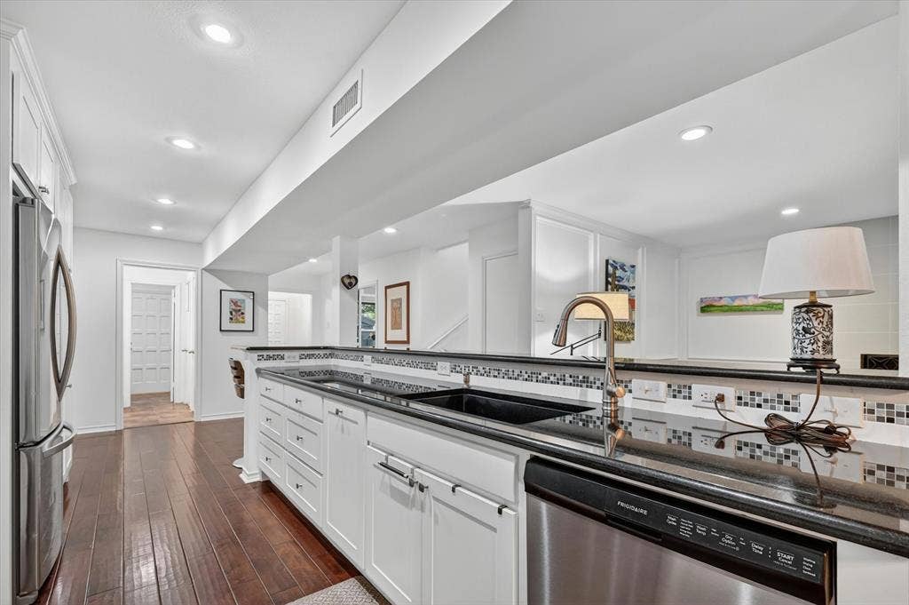 12627 Breckenridge Drive, #200, Dallas, TX 75230 Kitchen featuring white shaker-style cabinetry, dark stone countertops, mosaic tile backsplash, integrated stainless steel appliances, and wood-finish flooring
