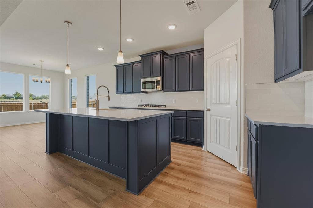 2109 Bluebird Lane, Anna, TX 75409 Kitchen featuring a center island, dark cabinetry, light countertops, stainless steel appliances, and wood-finish flooring