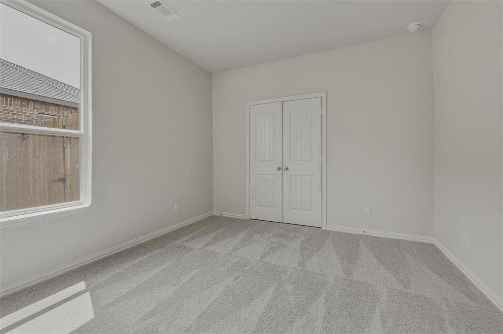 2109 Bluebird Lane, Anna, TX 75409 Bright secondary bedroom showcasing plank-style wood-finish flooring, abundant natural light from a large window, and dual closets with white panel doors for ample storage