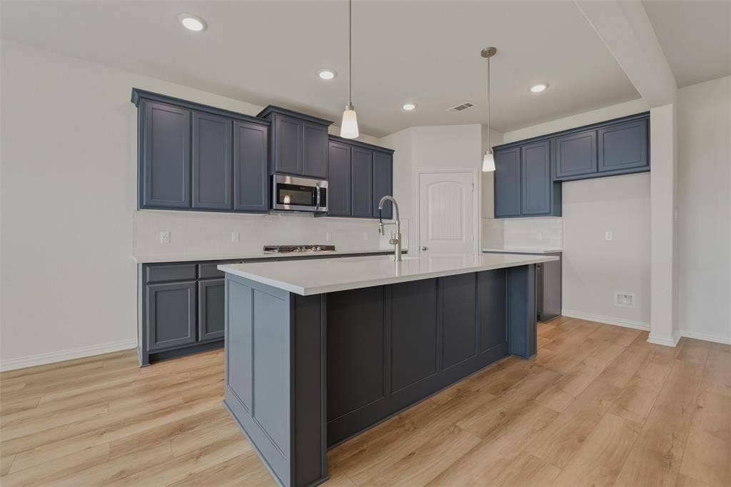 2109 Bluebird Lane, Anna, TX 75409 Kitchen featuring wood-finish flooring, dark cabinetry, light countertops, stainless steel appliances, and a central island with an integrated sink