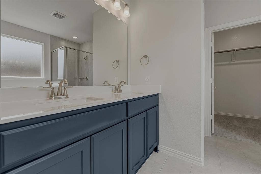 2109 Bluebird Lane, Anna, TX 75409 Dual vanity with dark blue cabinetry and white countertops, large mirror, and shower enclosure with glass panels