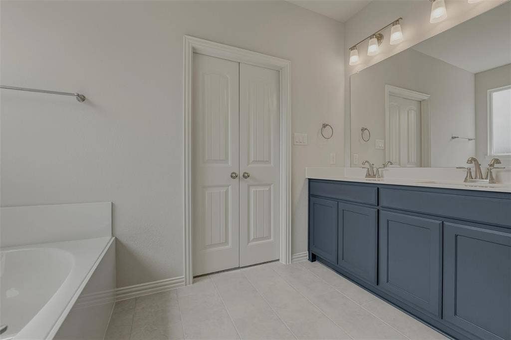 2109 Bluebird Lane, Anna, TX 75409 Dual-sink vanity with blue cabinetry and white countertops, large wall-mounted mirror, and a built-in bathtub