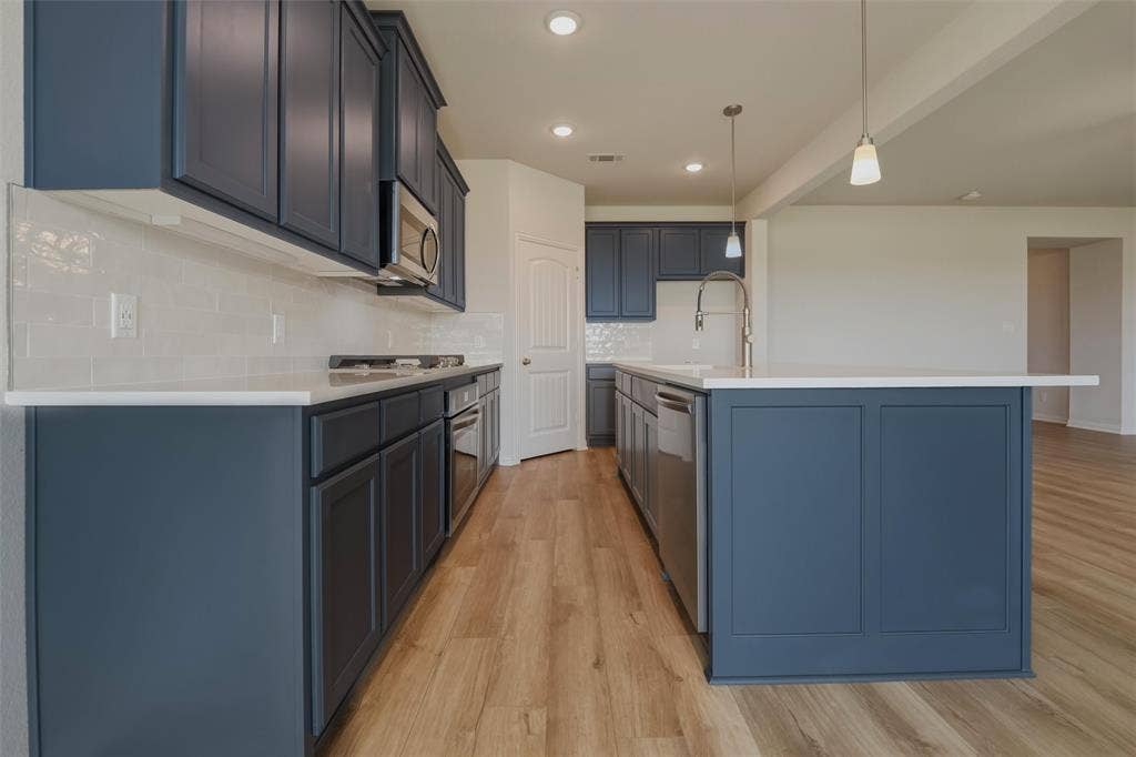 2109 Bluebird Lane, Anna, TX 75409 Kitchen featuring wood-finish flooring, dark blue cabinetry, light countertops, subway tile backsplash, and stainless steel appliances