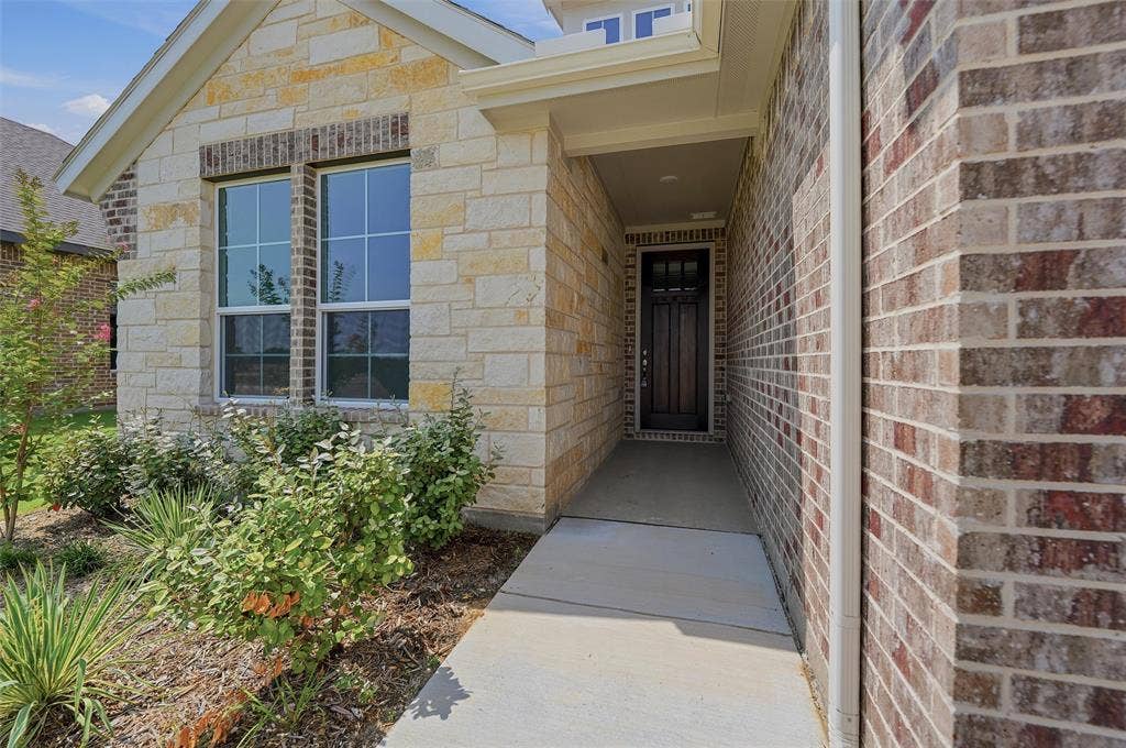2109 Bluebird Lane, Anna, TX 75409 Stone and brick exterior with a covered entry, dark wood-finish front door, and established landscaping