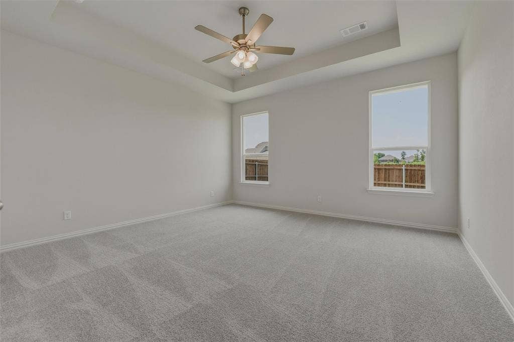 2109 Bluebird Lane, Anna, TX 75409 Spacious room featuring a tray ceiling, ceiling fan, two large windows, and wall-to-wall carpeting