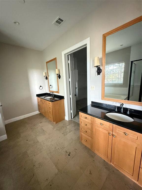 1025 Emerson Park Lane, Irving, TX 75063 Dual wooden cabinetry vanities with dark stone countertops, undermount sinks, framed mirrors, and wall-mounted light fixtures, finished with large-format tile flooring