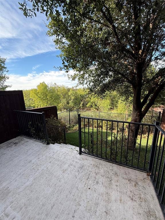 1025 Emerson Park Lane, Irving, TX 75063 Concrete patio featuring a black metal railing, wood privacy fencing, and a mature tree