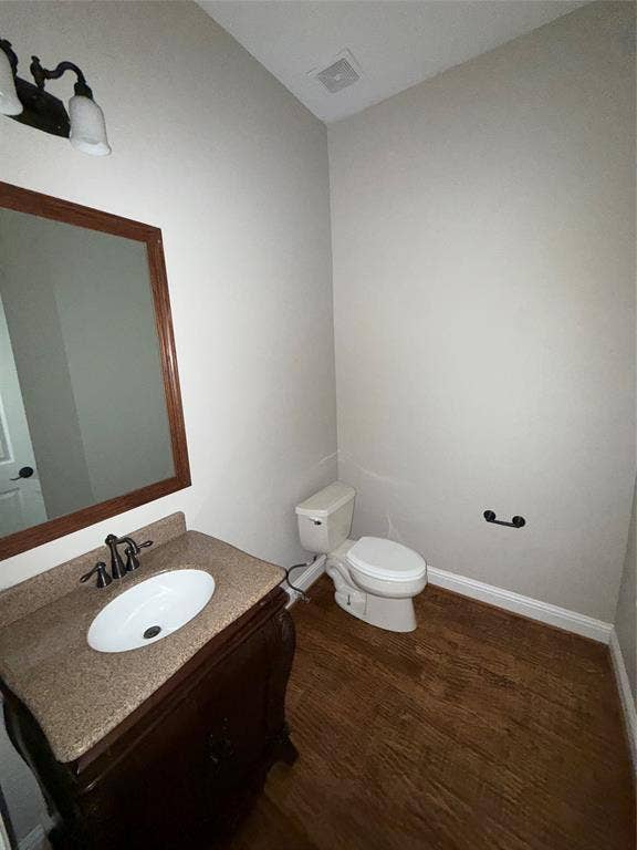 1025 Emerson Park Lane, Irving, TX 75063 Bathroom featuring a wood-finish vanity, solid surface countertop with an integrated basin, wood-finish flooring, and a wall-mounted vanity mirror with a decorative frame