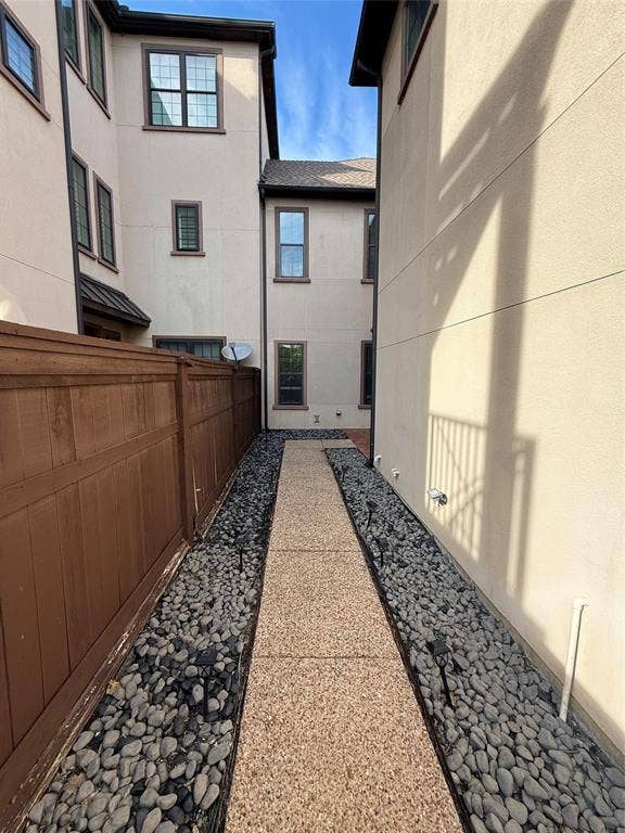 1025 Emerson Park Lane, Irving, TX 75063 Exterior side path featuring a textured aggregate walkway, decorative stone border, integrated landscape lighting, and a solid wood privacy fence
