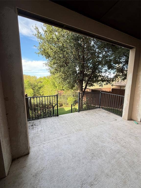 1025 Emerson Park Lane, Irving, TX 75063 Covered concrete patio featuring a black metal railing and a backdrop of mature trees