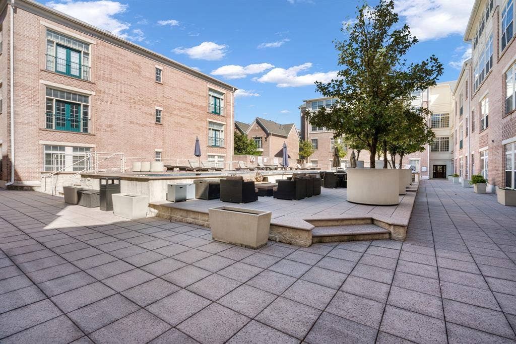 2305 Worthington Street, #103, Dallas, TX 75204 Paved courtyard terrace featuring brick building exteriors, tiered stone-finished hardscaping, and integrated concrete planters with mature trees