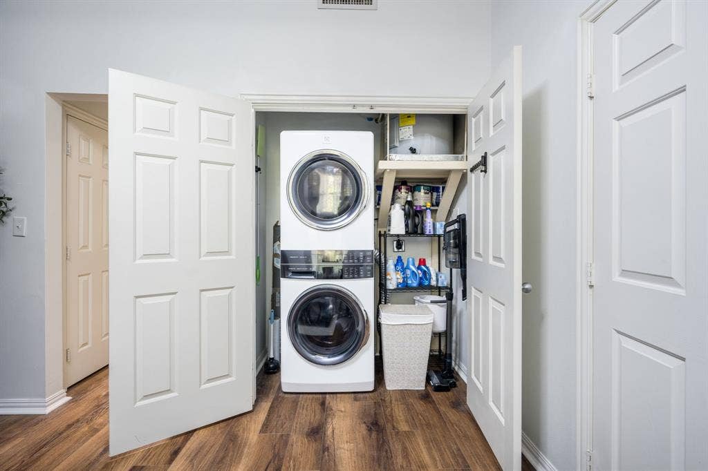 2305 Worthington Street, #103, Dallas, TX 75204 Laundry closet featuring stackable washer and dryer, wood-finish flooring, and recessed storage shelving