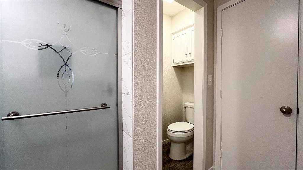 Frosted glass shower door with metallic handle, neutral wall tile, two-piece toilet, and built-in upper wall cabinetry