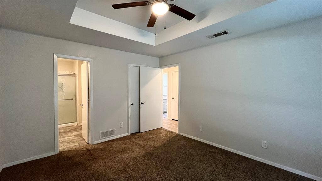 Tray ceiling featuring a central ceiling fan with integrated lighting, neutral wall finishes, and carpeted flooring
